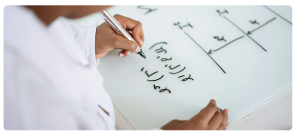 Engineer in white coat writes and equation on a whiteboard
