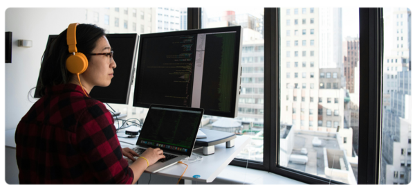 Engineer works on 电脑 code at a standing desk in front of large windows overlooking city